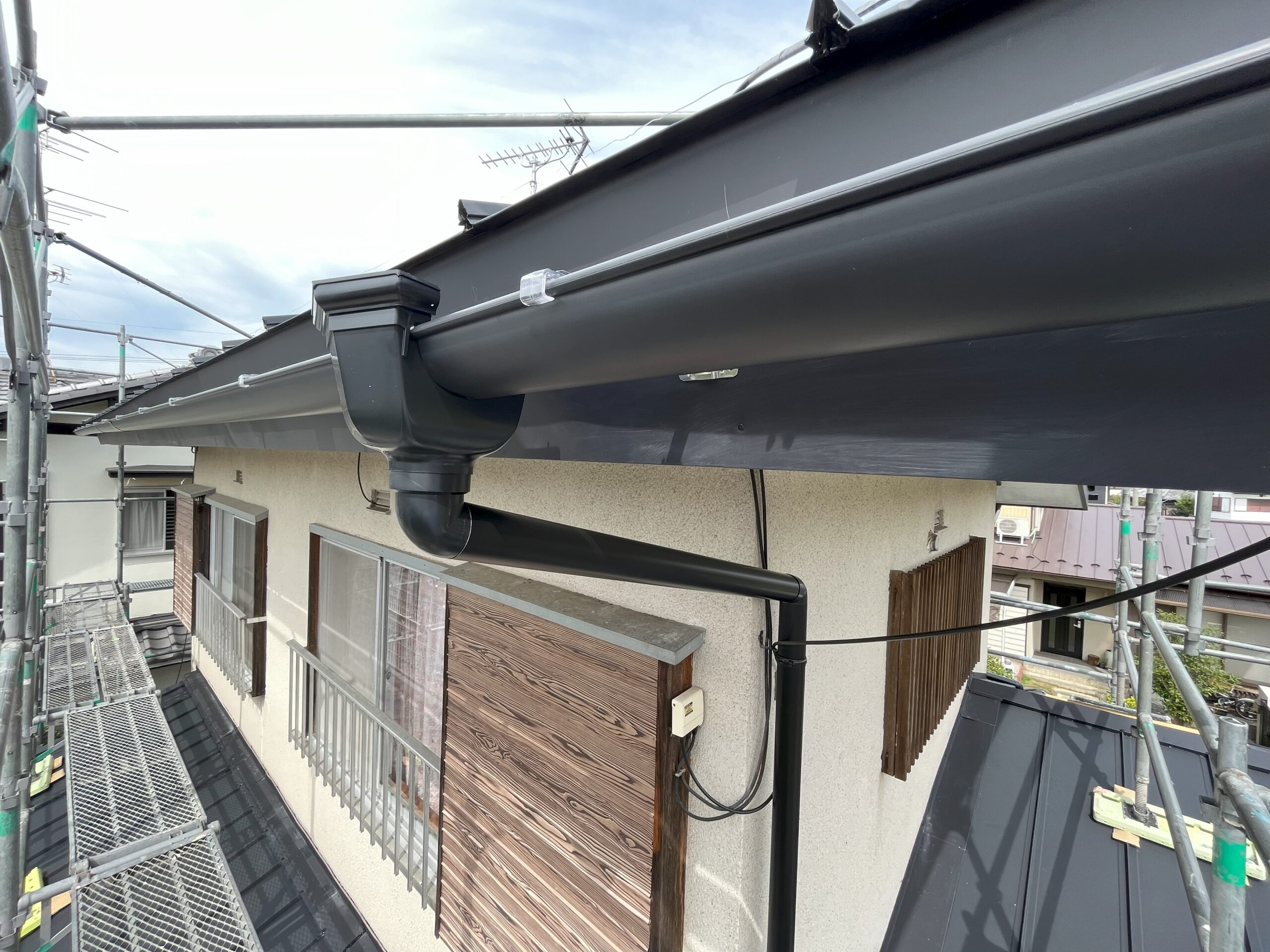 新しく設置された雨樋の実例。軒先に沿った軒樋、端の集水器、外壁を下る竪樋が一式そろっている屋根の写真