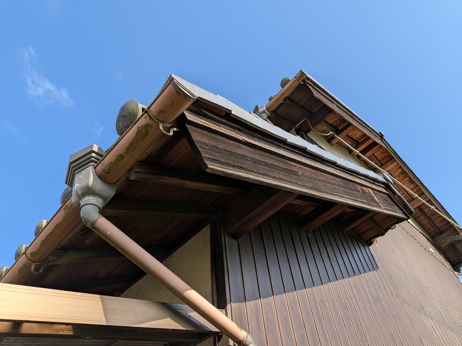 妻側の破風板の実例。木製の破風板が経年で色あせ、軒先に雨樋が取り付けられている屋根の写真