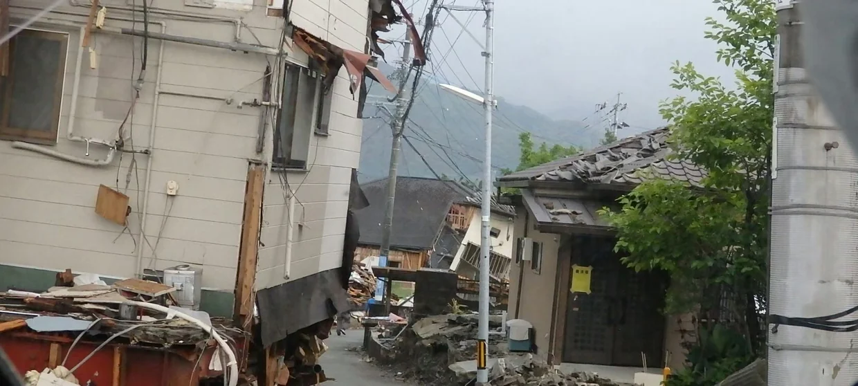 2016年熊本地震のあとの益城町の街並み。1階部分が崩れた2階建ての建物と、その先に残っている瓦屋根の住宅