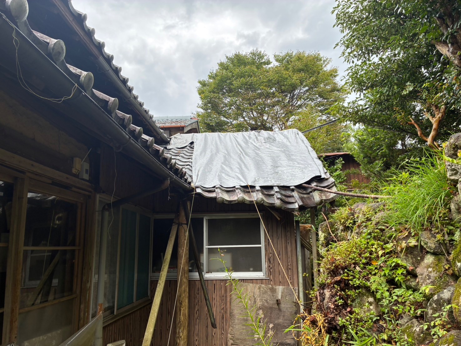 【施工前】主屋に接する下屋の瓦屋根。軒先が垂れ下がり、応急処置のシートが掛けられた状態